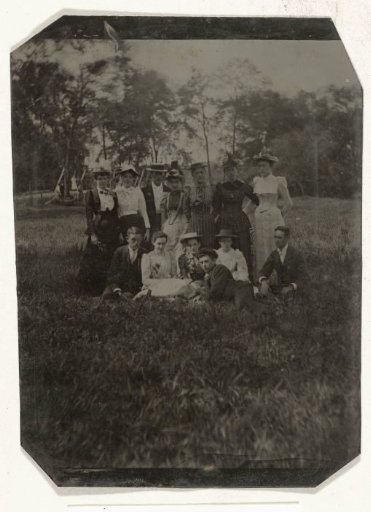 Group portrait of nine women (including Estelle Hopping) and four men standing and sitting in the grass