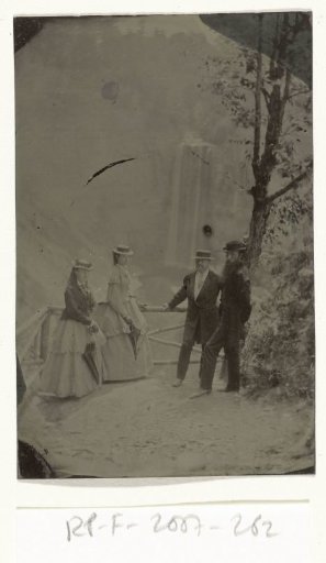 Two men and two women standing on a sandy path, with a waterfall in the background (Taughannock Falls), NY, United States