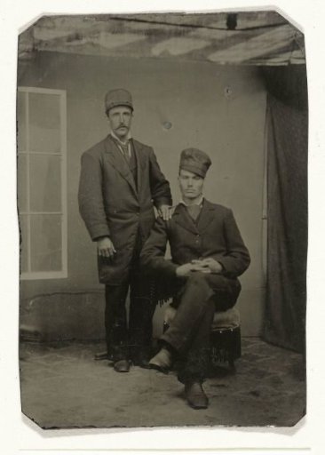 Portrait of two men in a studio in front of a painted backdrop