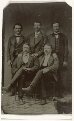 Group portrait of five men, standing and sitting in a studio (at the far right, two feet of another person)