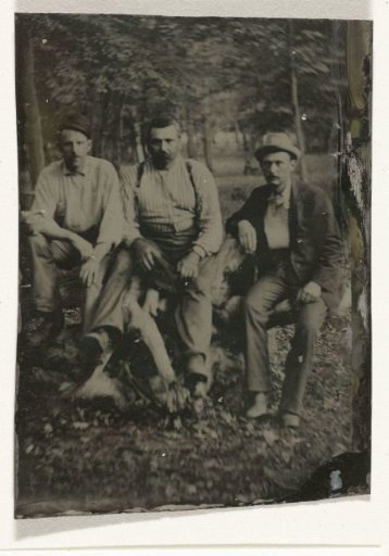 Portrait of three men, sitting (on a tree stump?) in a forest