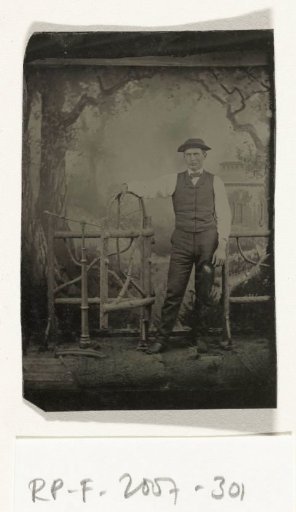 Portrait of a Man, Standing Before a Painted Backdrop (Forest and House) and a Wooden Fence, with a Neck Rest on the Left