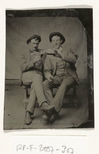 Portrait of two men, one pouring drink from a bottle into a glass for the other