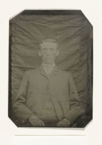 Portrait of a man seated before a plain, wrinkled backdrop