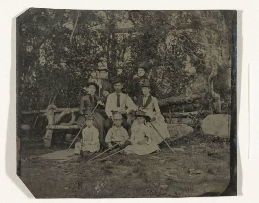 Group portrait of a man, four women, a boy and two girls, standing and seated in a landscape (Adirondacks, United States?), with walking sticks