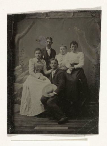 Group portrait of two men and three women, standing and seated before a painted backdrop (tree, rocks)