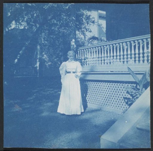 Woman in a long dress standing before a wooden house, United States