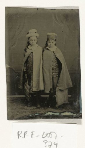 Portrait of Two Girls with Hats and Cloaks, Standing in a Studio Setting