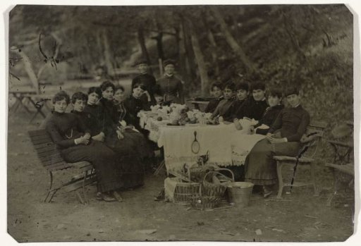 Group portrait of fourteen women around a table during a picnic outdoors