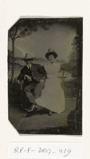 Portrait of a man and a woman (Chas and Bo) sitting in front of a painted backdrop (lake with trees, Puddin Bay)