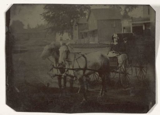 Man and Woman Sitting in a Carriage with Two Horses in Front, with Wooden Houses in the Background