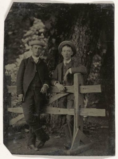 Two Men Standing by a (Faux) Wooden Fence, Near Trees Outdoors