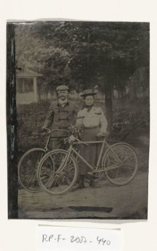 A Man and Woman Standing with Their Bicycles Outdoors, with a Bunch of Flowers