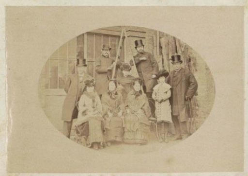 Group portrait of four men, four women and a girl standing by a barn in France
