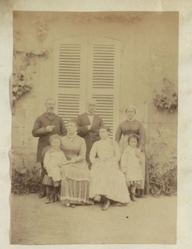 Group portrait of two men, three women and two children standing before a house in France