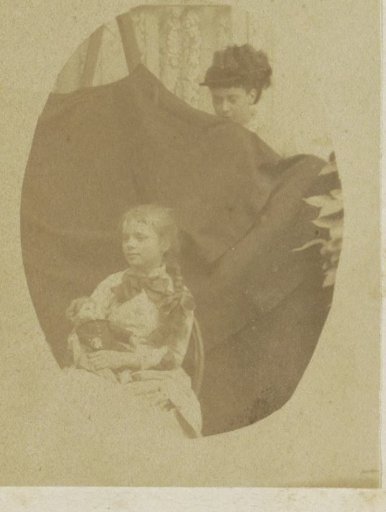 Portrait of a child with a doll, behind her a woman holding a background cloth