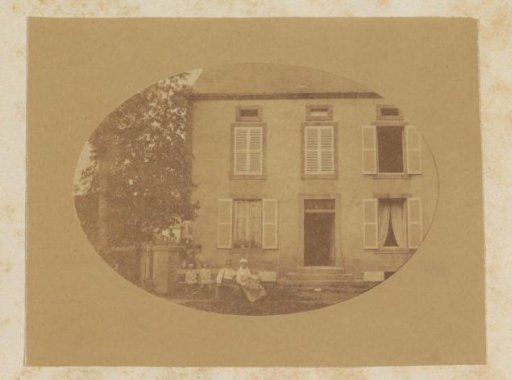 Man, woman and children seated in front of a country house in France