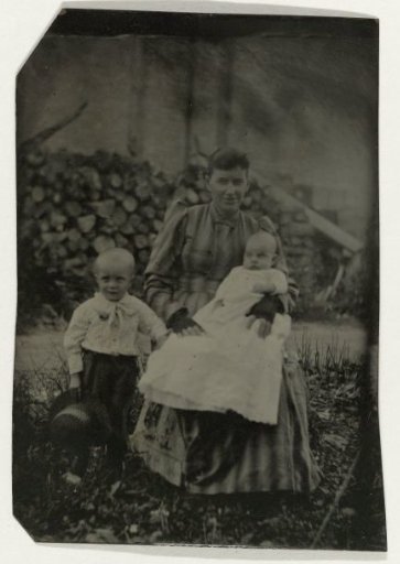 Woman with Two Children Posing Outdoors, with a Stack of Wood in the Background