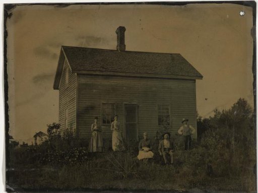 Two men and three women in front of their wooden house