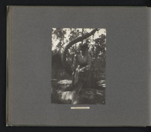 Portrait of a woman crouching in a pine forest in the Bahamas, a bottle of wine on a stone before her
