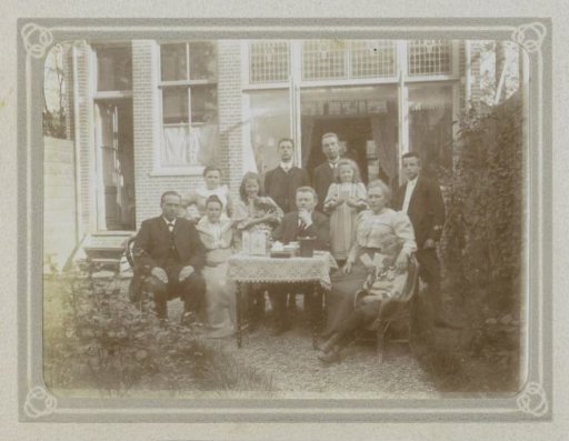 Group of men, women and children at a table behind a house