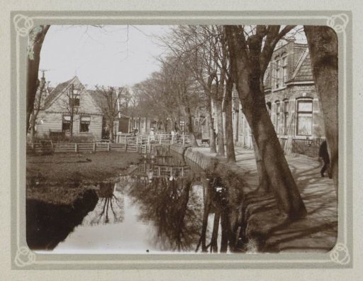Village street with houses, a ditch, and children with bicycles on a bridge