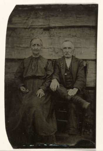 Portrait of an older man and woman sitting in front of a wooden wall or fence