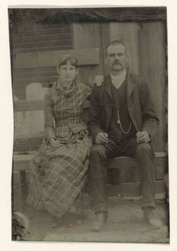 Portrait of a man and a woman sitting on a bench in front of their house (?)