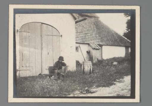 Boy seated in front of a farmhouse