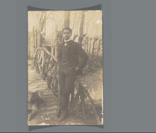 Portrait of Frédéric Dumas standing by a small bridge outside with a dog