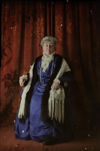 Portrait of a woman in a blue dress on a chair against a red background