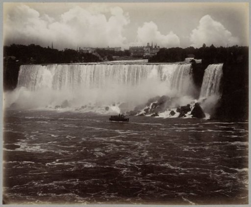 View of Niagara Falls with a boat downstream and buildings on the horizon