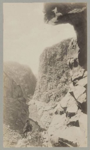 Man in a North American canyon with (presumably) a railway line in the distance