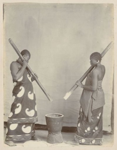 African women in long robes pounding in a mortar