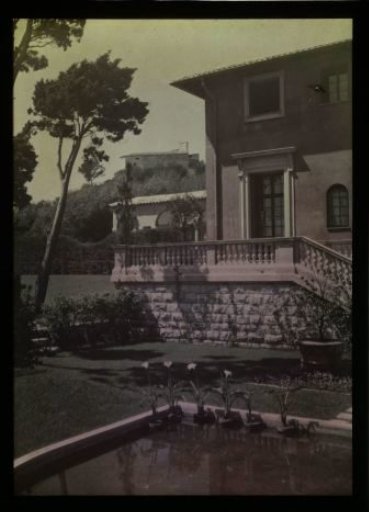 Pink stucco house, with a garden and pond in the foreground