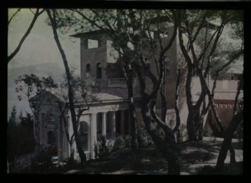 Part of a pink stucco house with portico and trees in the foreground