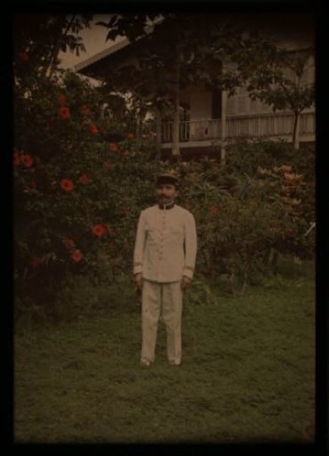 Man in uniform, in a garden with a house in the background