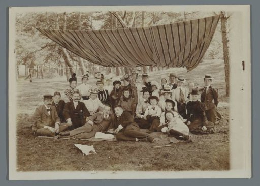 Group portrait of the Geertsema family with Karel van den Berg and Frans and Poppie van den Berg, sitting on the grass in the forest under a striped awning