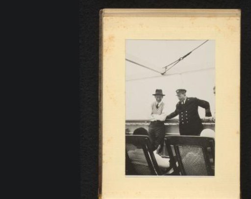 Two men leaning against the railing of a ship, with deck chairs in the foreground