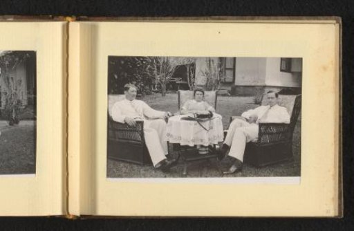 Woman with two men on either side, seated at a table in a garden