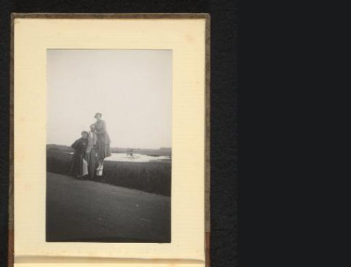 Man with two women on either side, the woman on the right standing on a post by the road