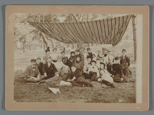Group portrait of the Geertsema family with Karel van den Berg and Frans and Poppie van den Berg, sitting on the grass in the forest under a striped awning