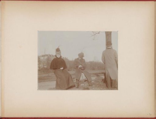 Young couple, woman with a feathered hat, caught on a bench in a park, man from behind a tree addresses the woman, the other man walks away, photo story 2