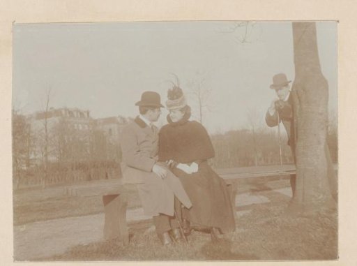 Young couple, woman with a feathered hat, in an affectionate pose on a bench in a park, man peering from behind a tree, photo story 1