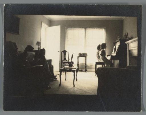 Interior with a family on the sofa and two girls behind the piano