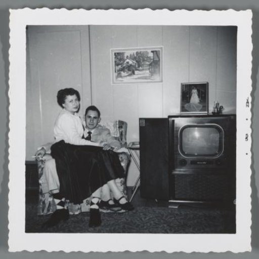 Portrait of a woman on her husband's lap beside the television cabinet
