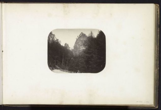 Mountain landscape with a road and steep rock wall, possibly in the Alps