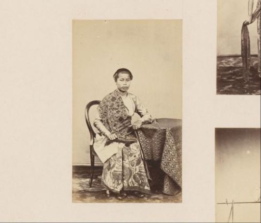 Portrait of an Indonesian woman, seated at a table in a long robe
