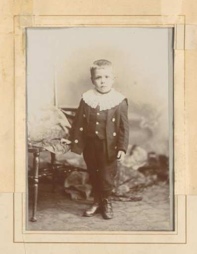 Portrait of a standing boy with a lace collar beside a chair