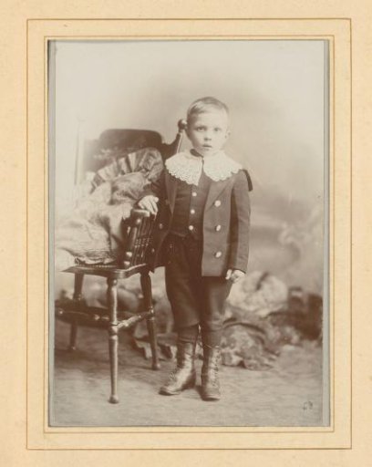 Portrait of a standing boy with a lace collar beside a chair